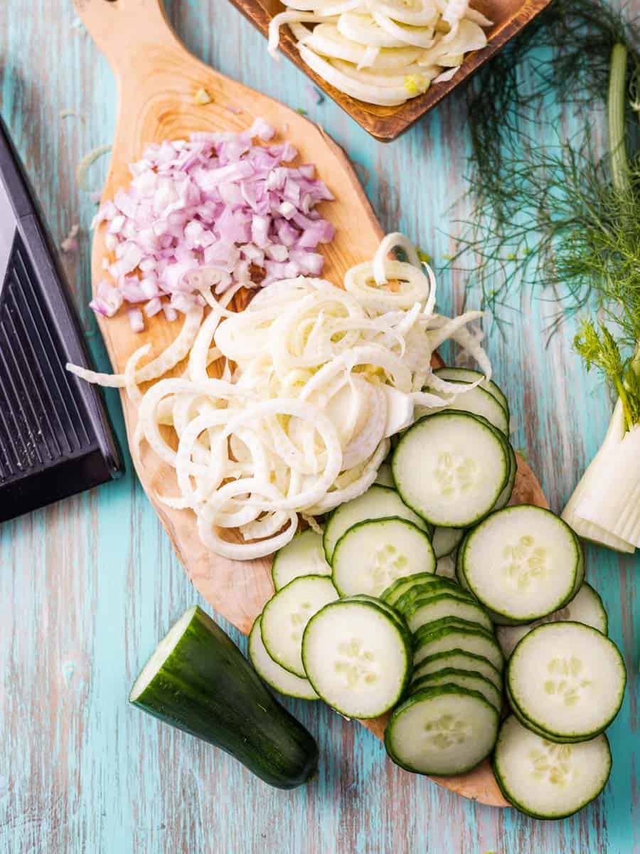 Sliced cucumbers, fennel, and diced shallots on a cutting board