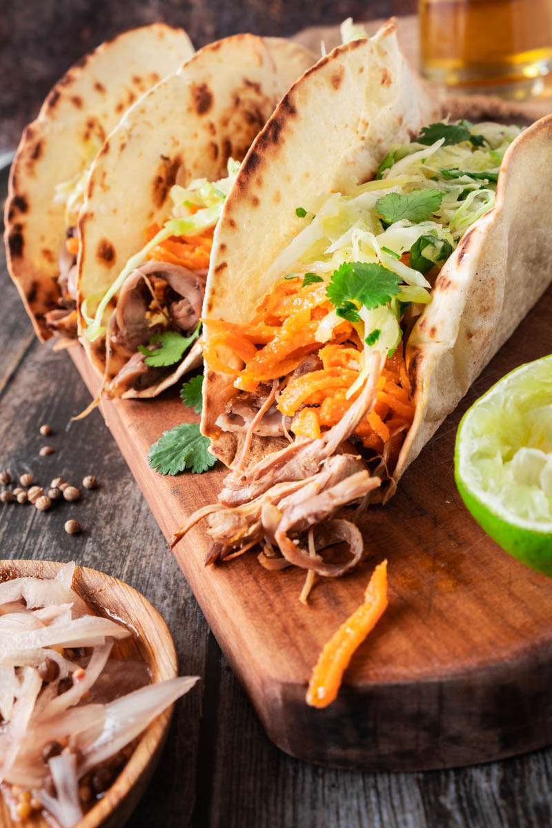 Lamb Tacos with Pickled Shallots, Cabbage Slaw, and Carrot Salad on wooden board.