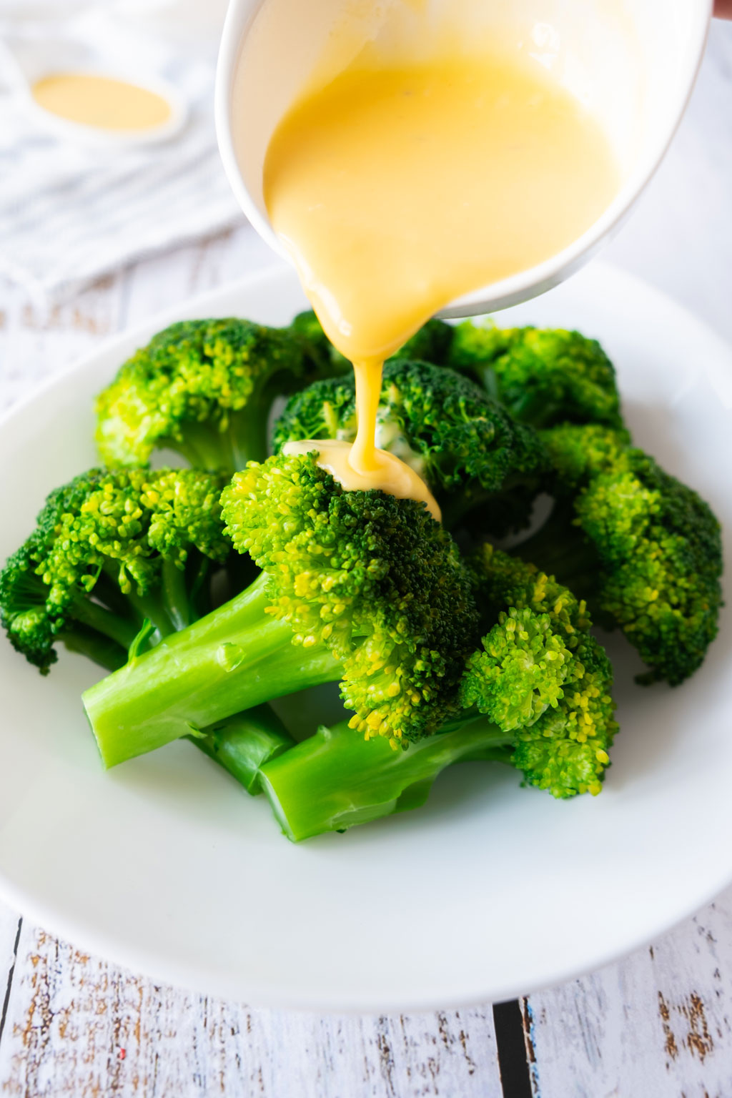Hollandaise sauce being poured on brocolli.