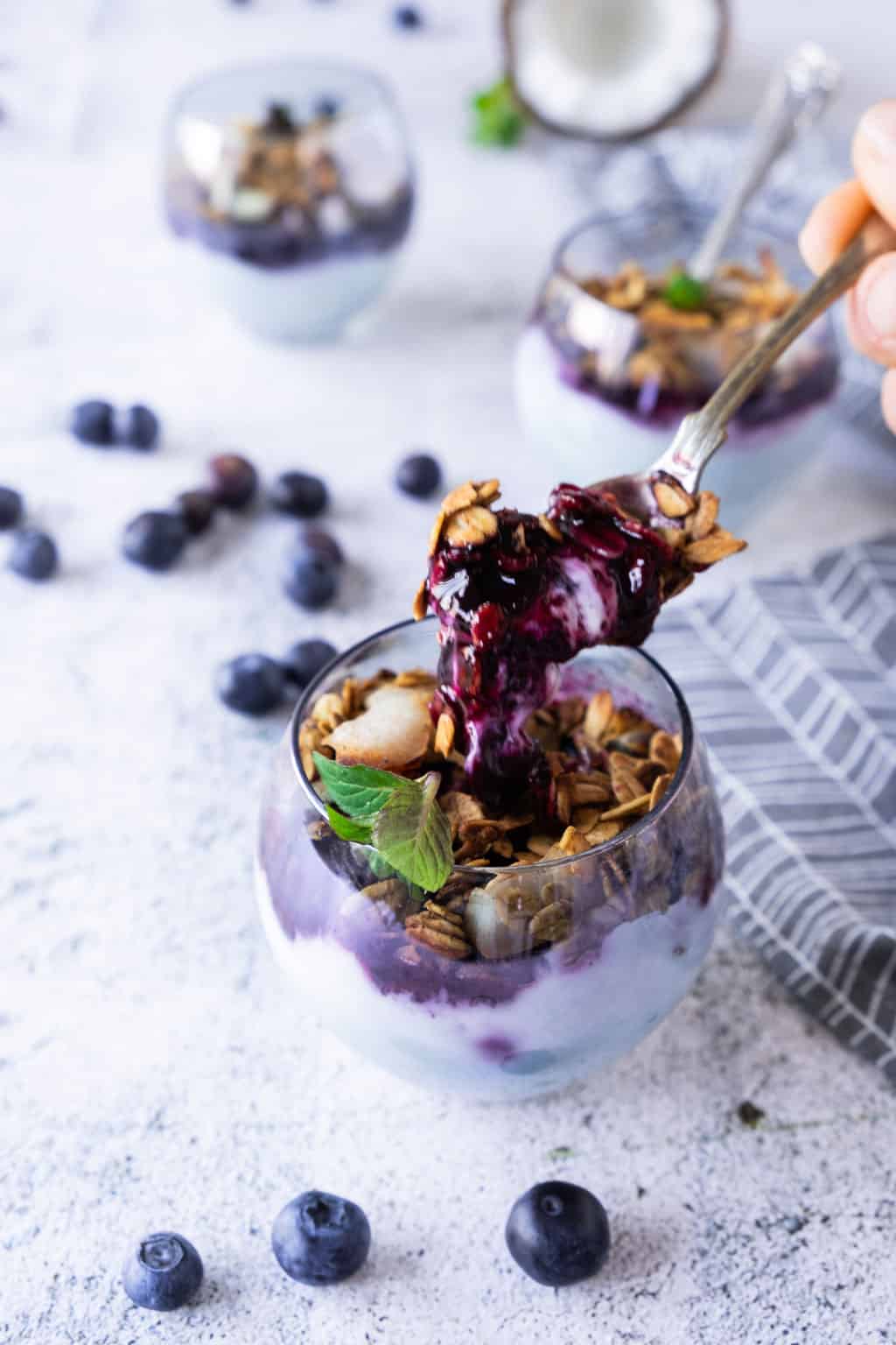 Spooning yogurt, blueberry compote, and granola.